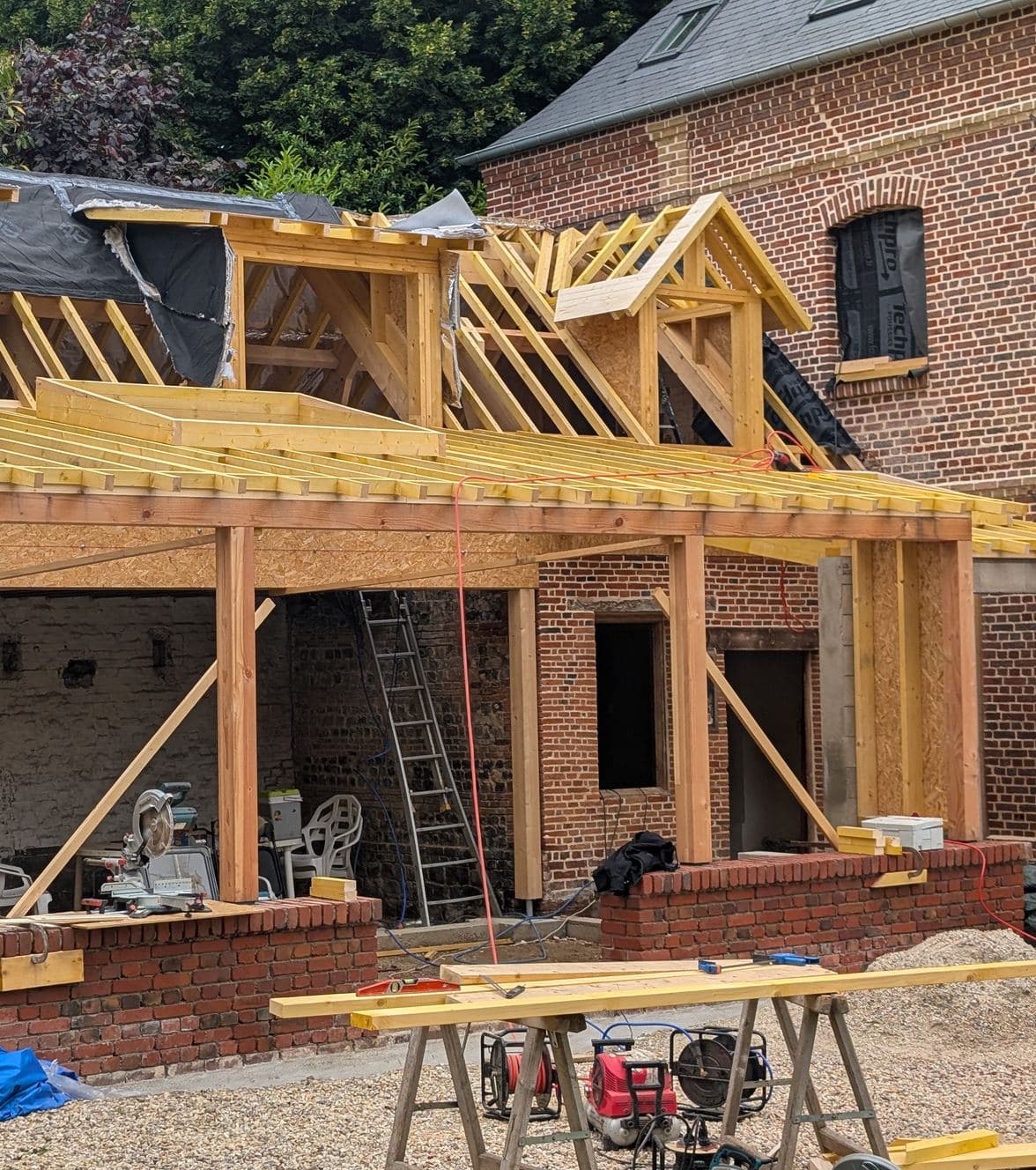 Structure bois poteaux-poutres d’une extension montée contre une maison en brique
