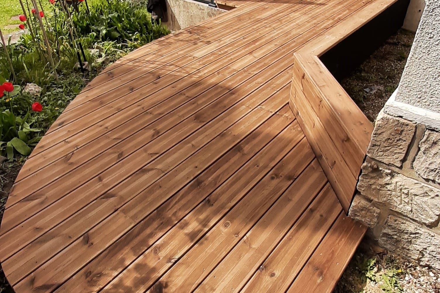 Terrasse en bois aux lames cintrées, bordée d’un muret de pierre