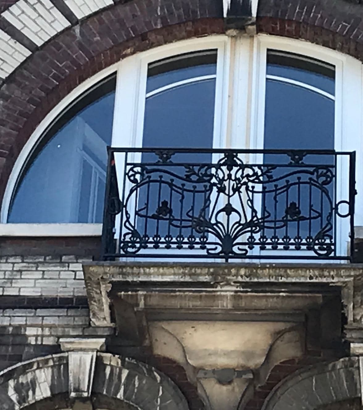 Fenêtre cintrée sur mesure posée dans une baie en brique, devant un balcon en ferronnerie