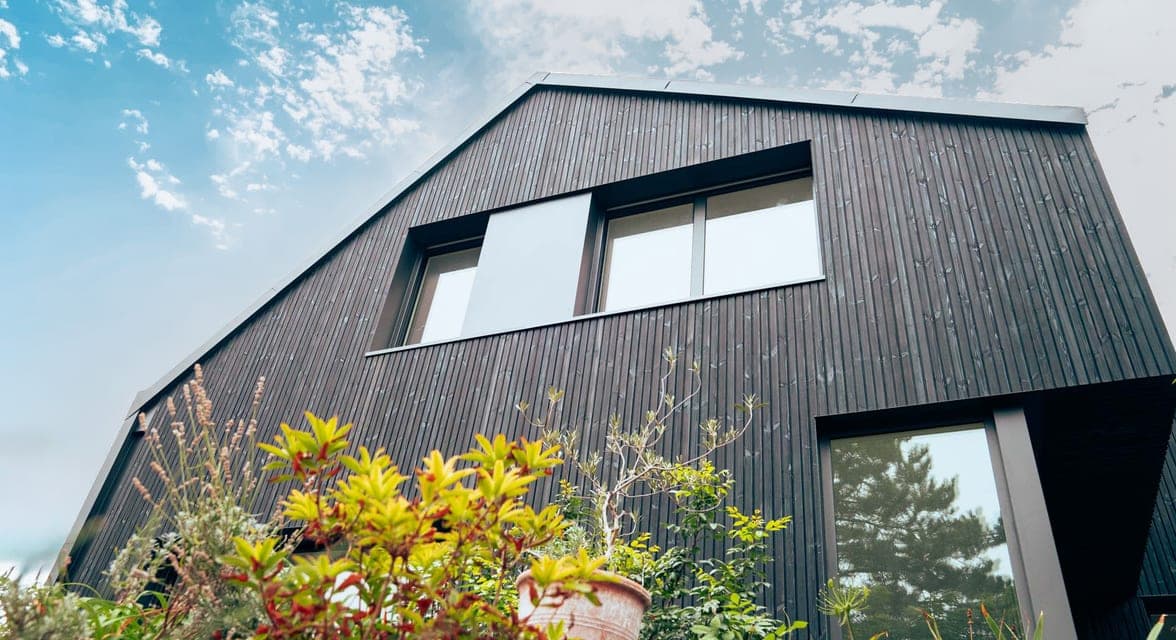 Extension bardée de bois teinté noir, sa toiture à faible pente