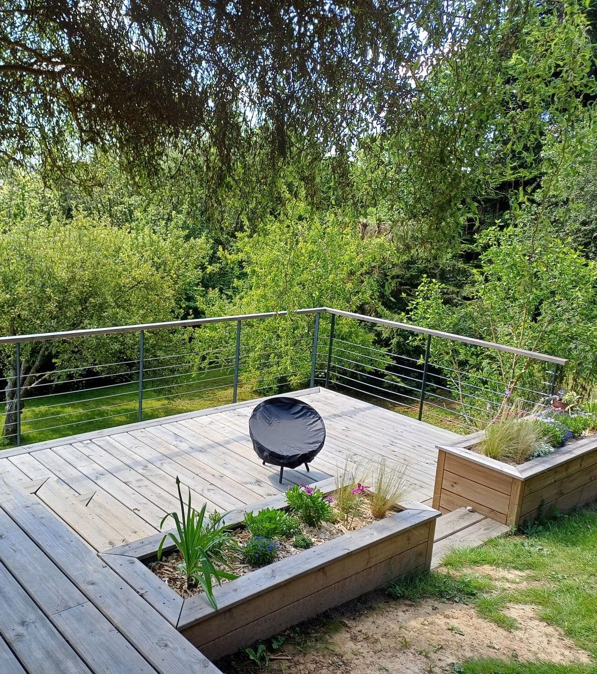 Terrasse en bois ouverte sur un jardin, bordée d’une jardinière et d’un garde-corps à câbles